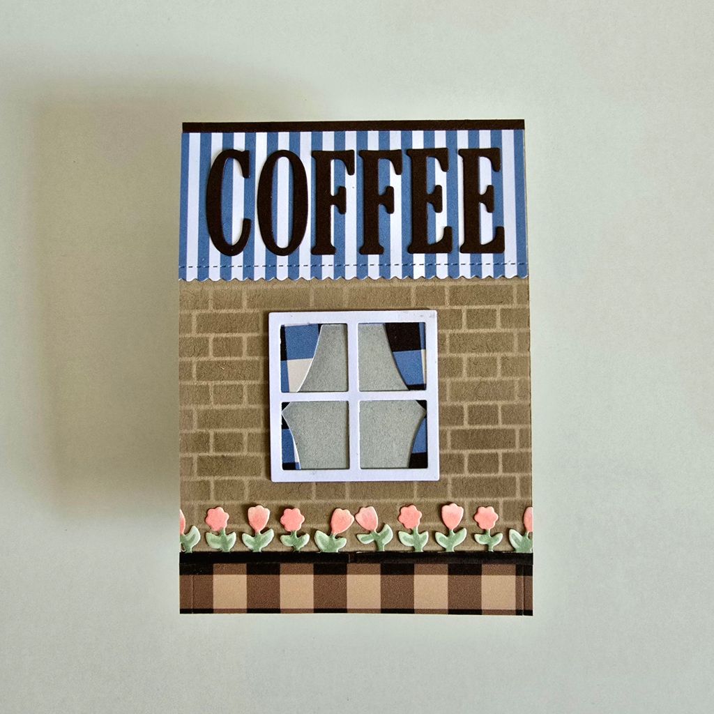 A stunning handmade card for coffee lovers, featuring a coffee shop front on the cover and an interactive pop-up scene of a couple sipping coffee inside.