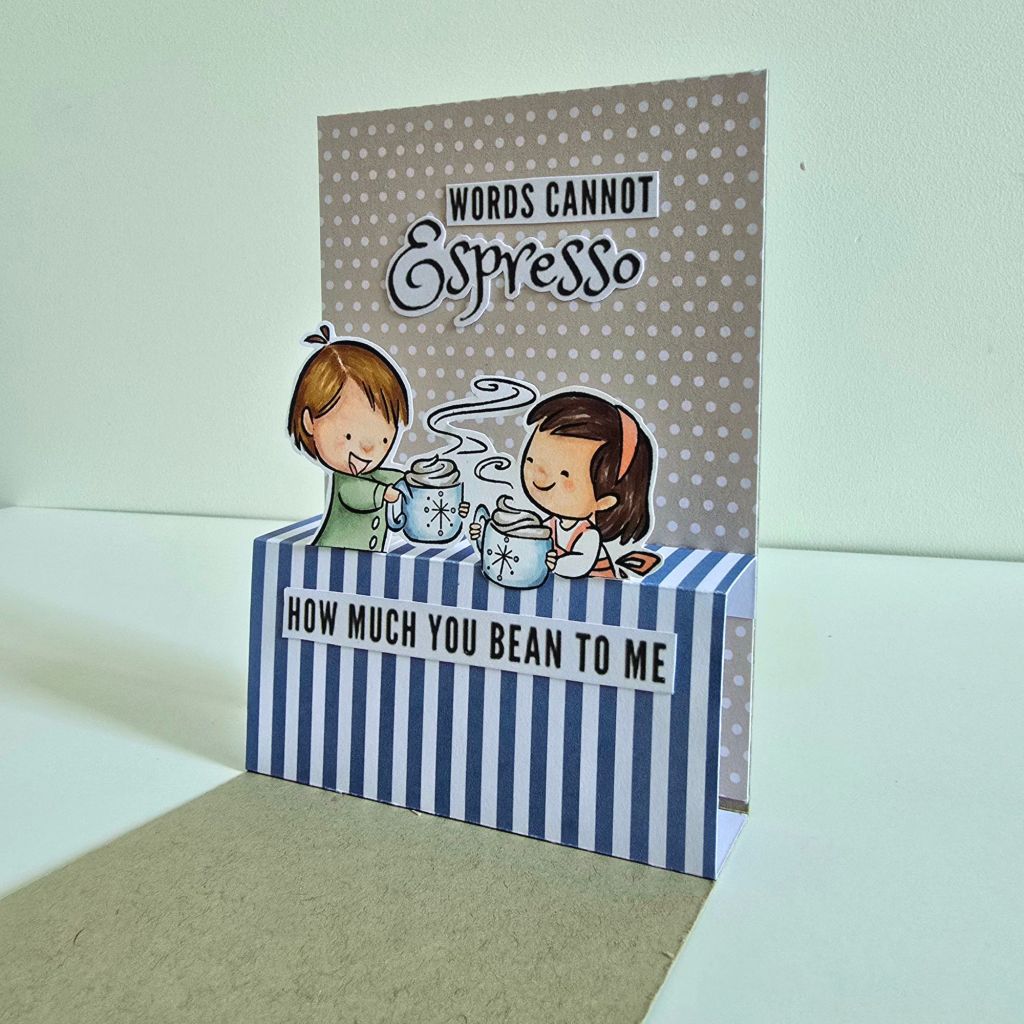 Charming handmade coffee-themed card in brown and blue tones. The front resembles a cozy café entrance, and opening the card reveals a pop-up couple sharing a heartwarming coffee moment.